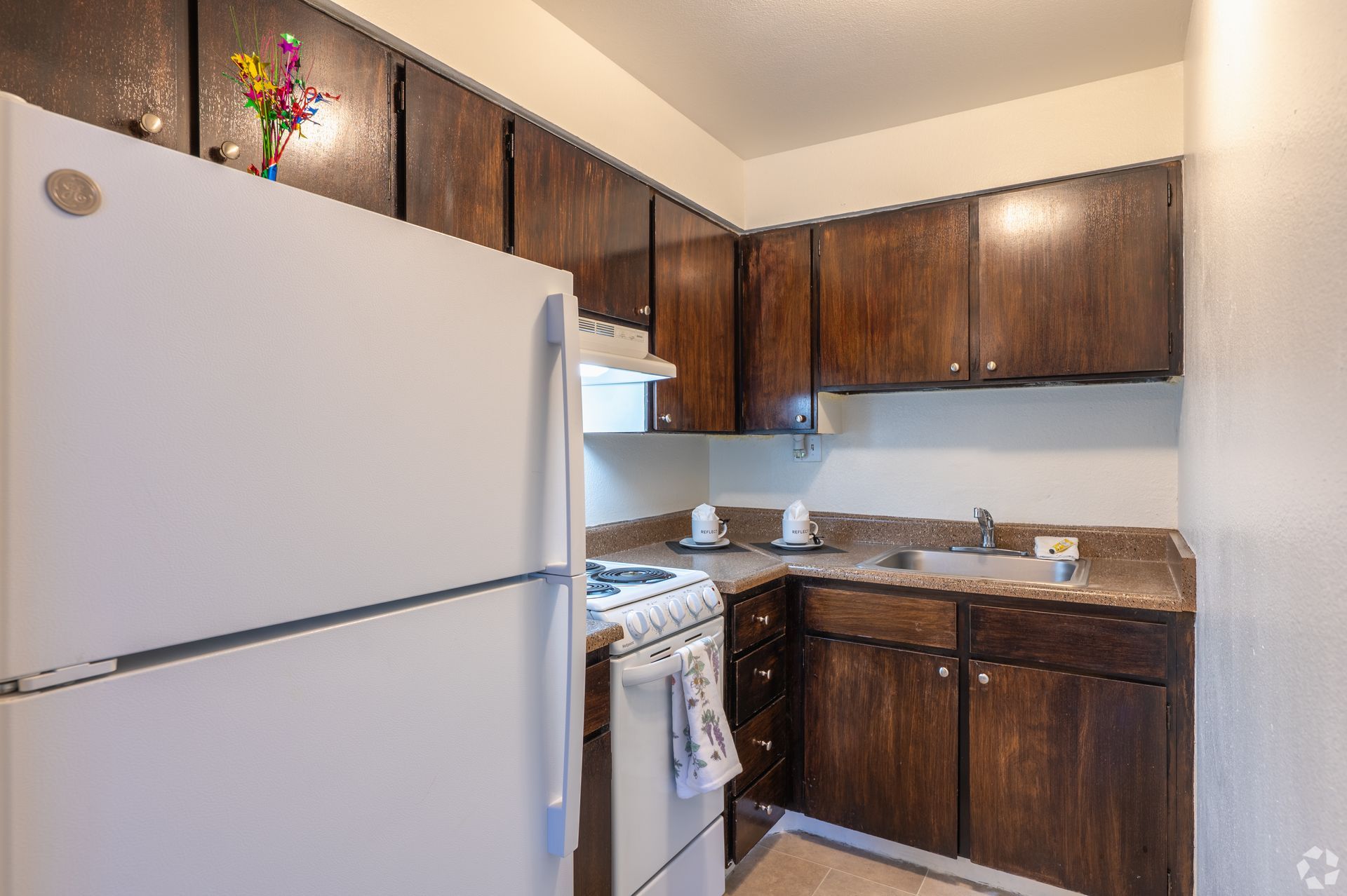 Small kitchen with white refrigerator, stove, and dark wooden cabinets.