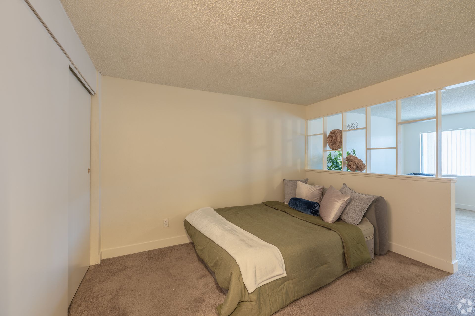 Bedroom with a green bedspread, beige carpet, and large windows letting in natural light.