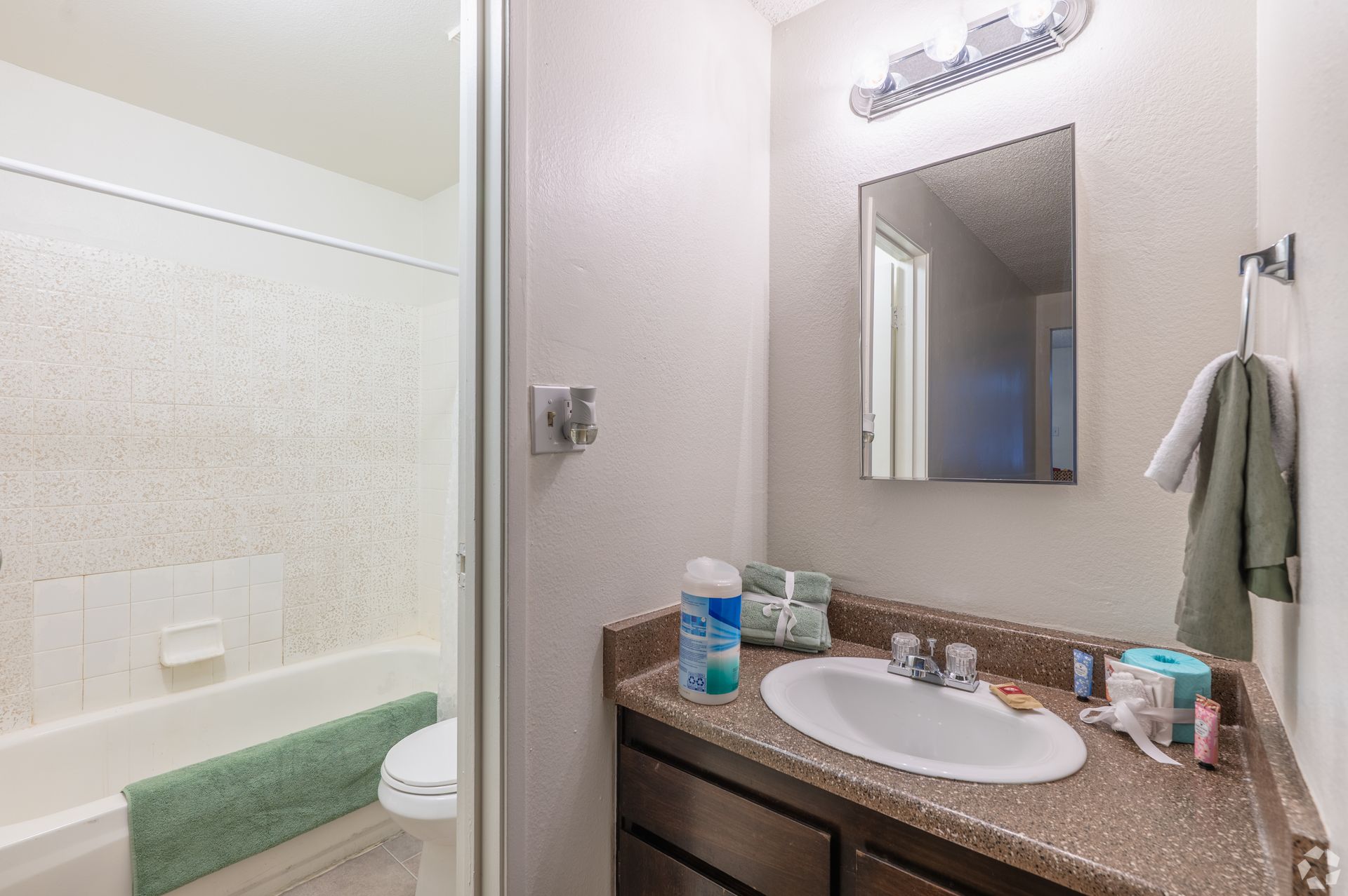 Small bathroom with a sink vanity, mirror, bathtub, and green towels on a neutral wall.
