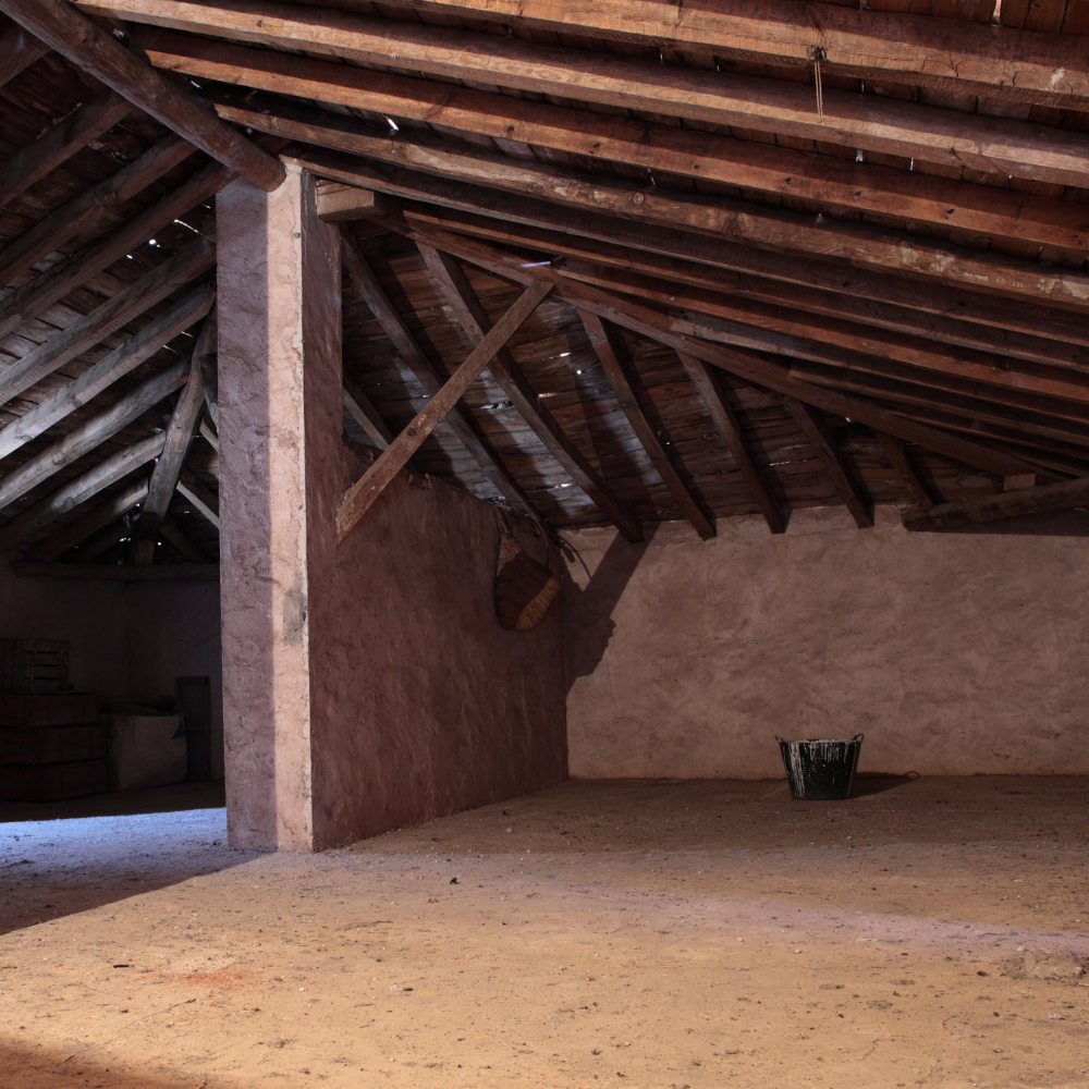 an empty room with wooden beams and a bucket on the floor