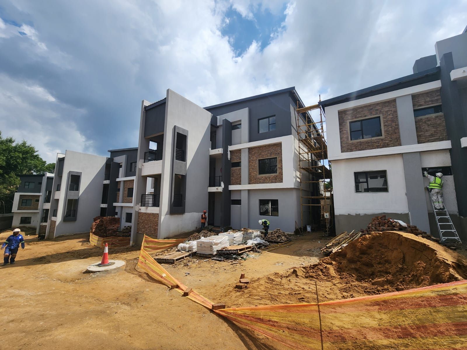 Modern apartment buildings under construction with dirt piles and a partly cloudy sky