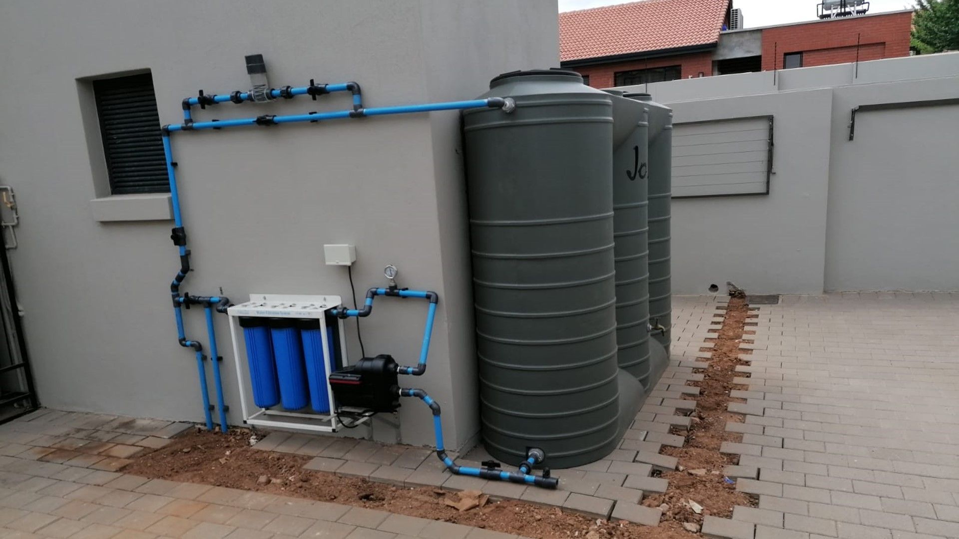Outdoor water tank and filtration system beside a building on a rooftop terrace.