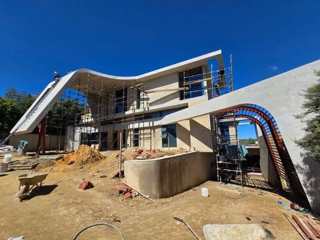 Modern house under construction with scaffolding, exposed framing, dirt yard, and blue sky