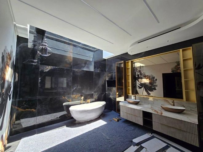 Modern bathroom with black marble walls, a freestanding tub, dual sinks, and warm backlit mirrors