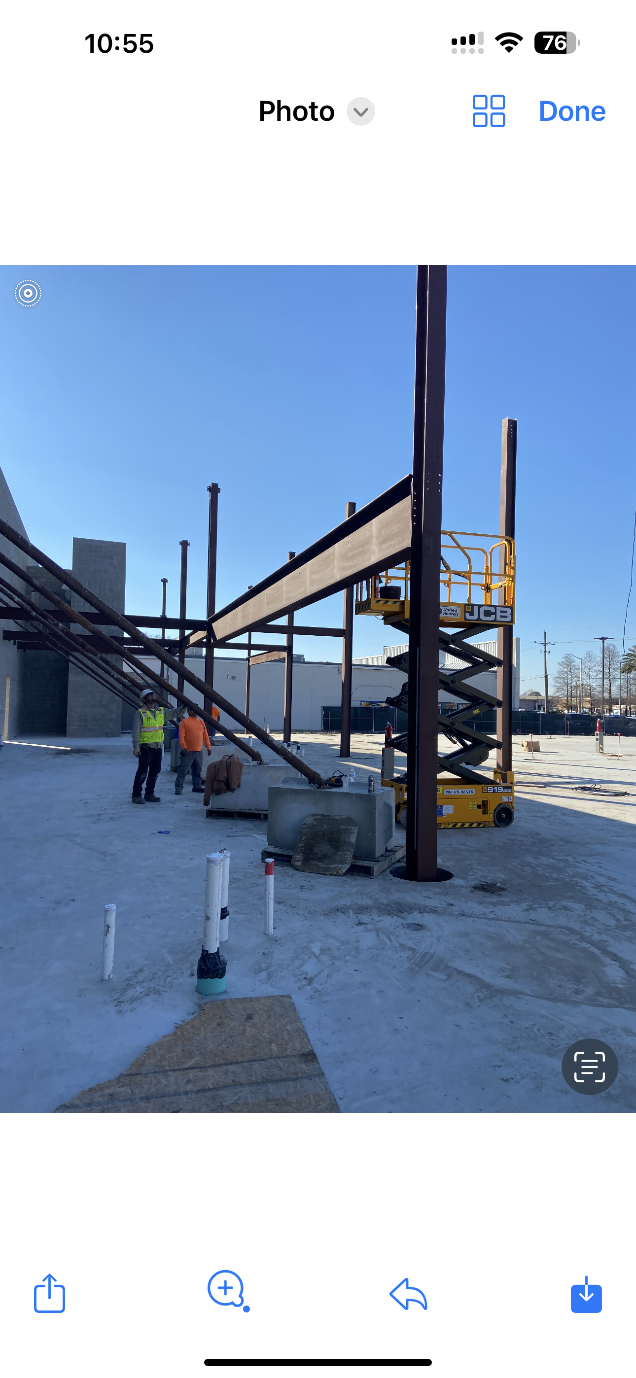 Workers stand near steel beams and a yellow scissor lift at an outdoor construction site on a sunny day.