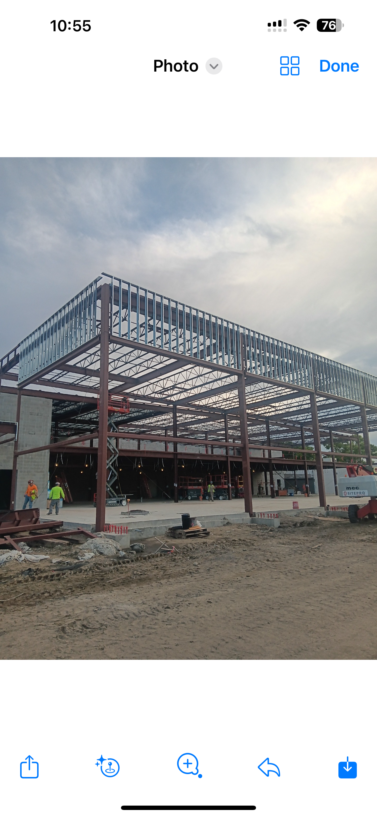 A construction site shows an unfinished building with a steel frame and a partially completed metal roof structure.