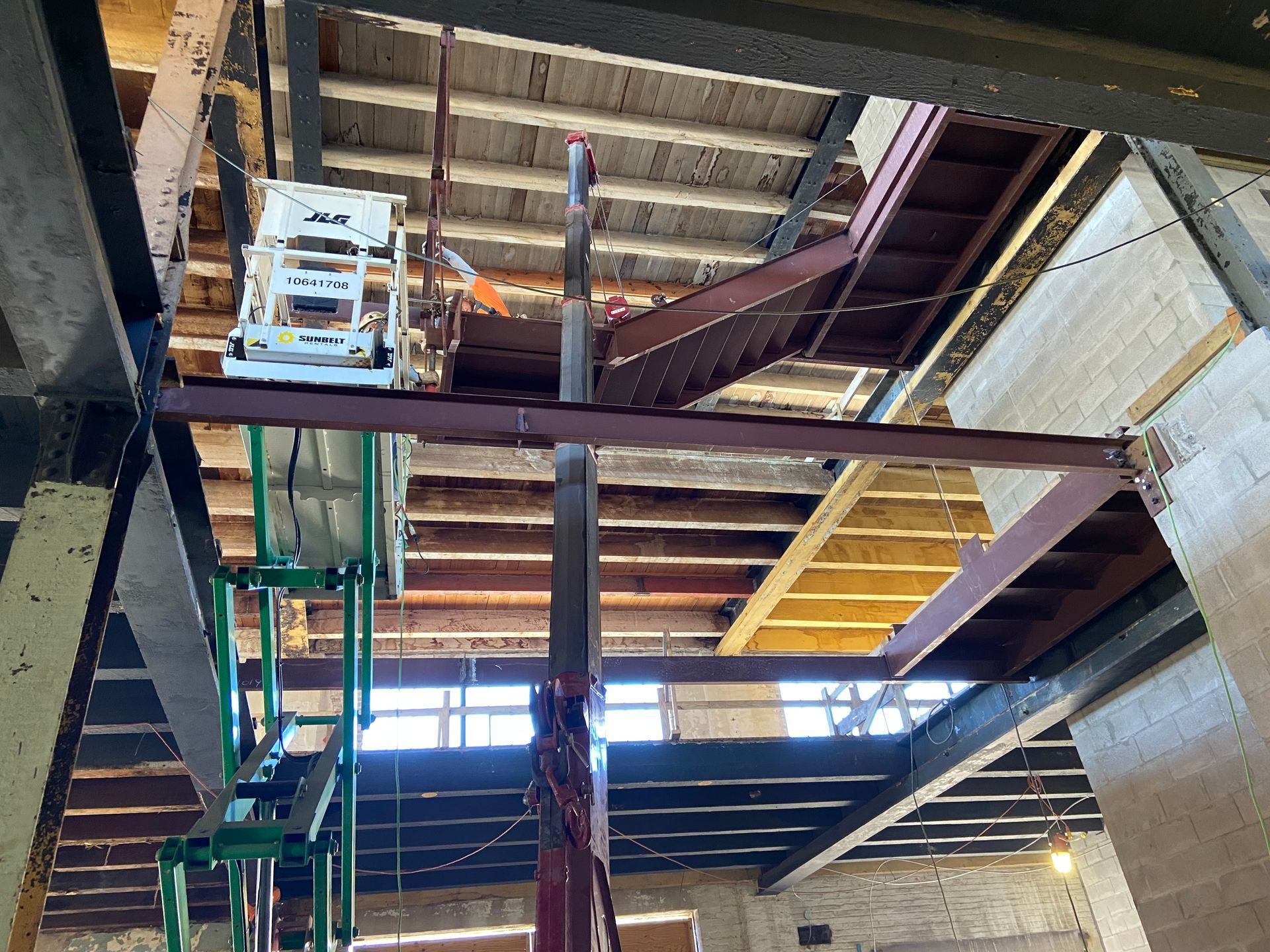 A view looking up at a building interior under construction, featuring exposed wooden joists, steel beams, and a lift.