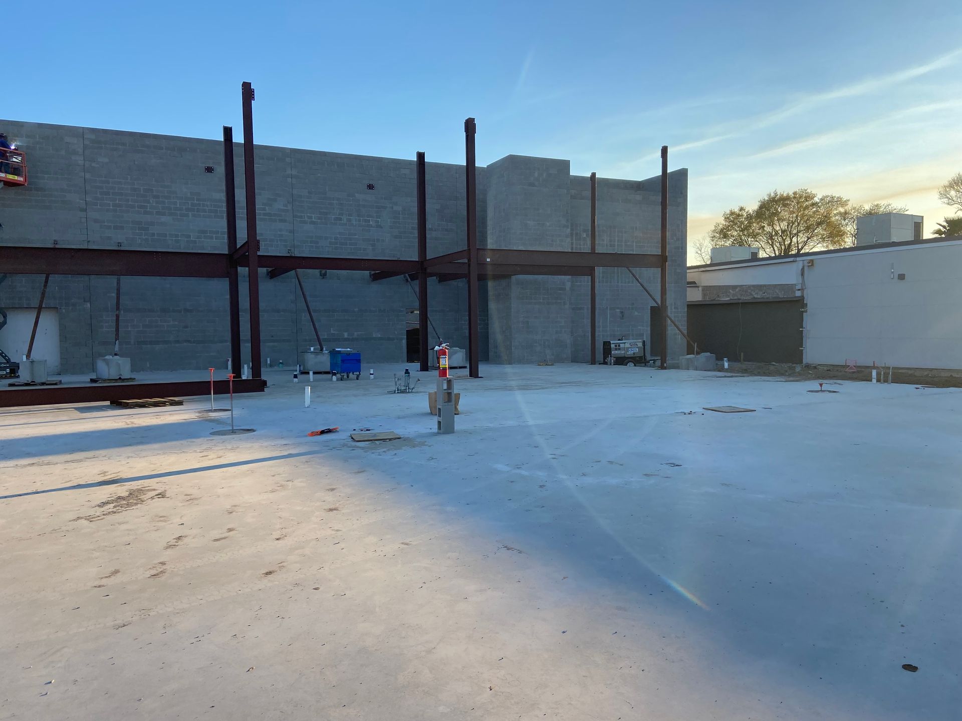 Construction site with steel beams, concrete walls, and open space, under a blue sky.