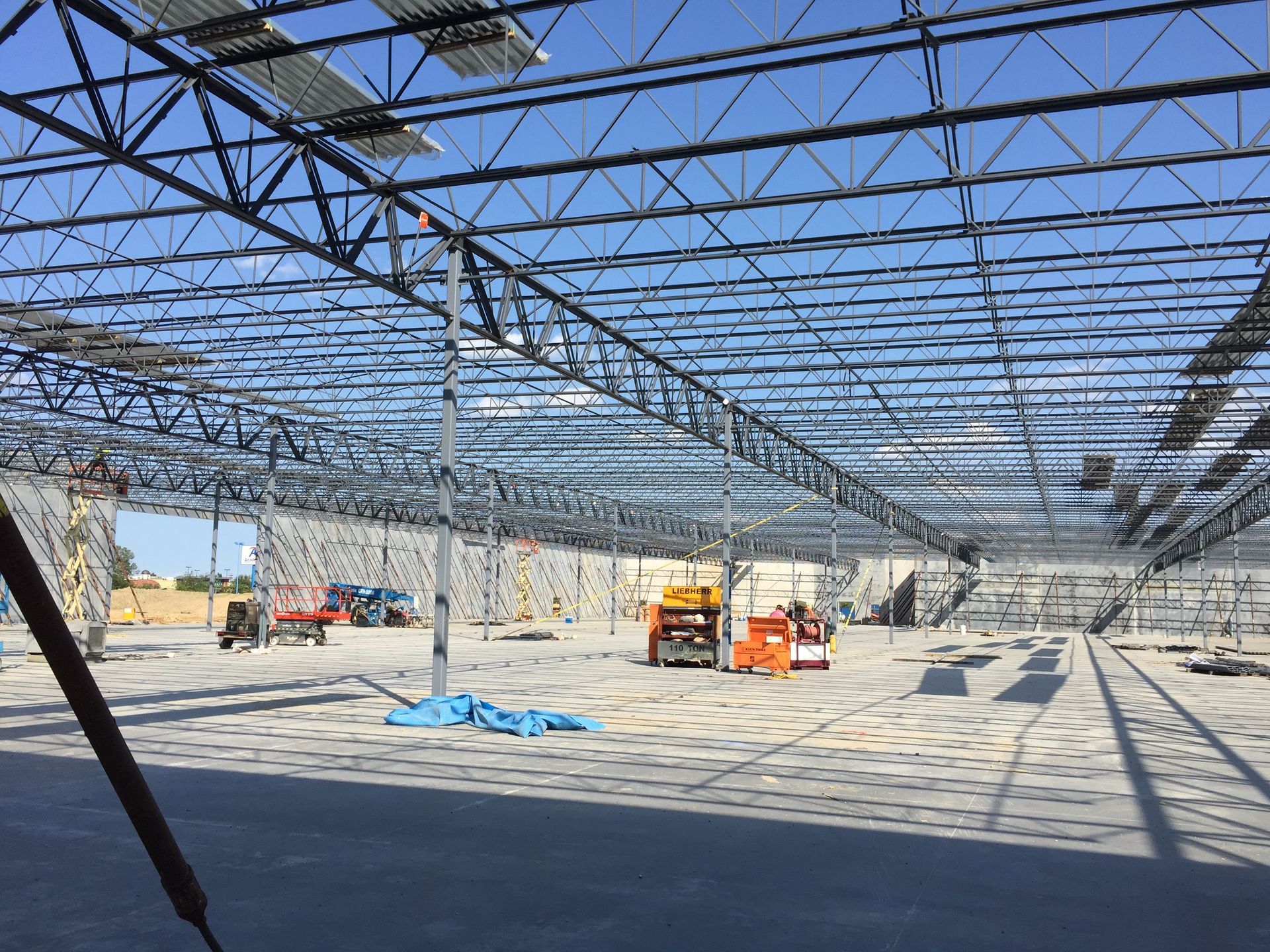 Interior view of a building under construction, featuring an open floor and a high steel-truss roof structure.