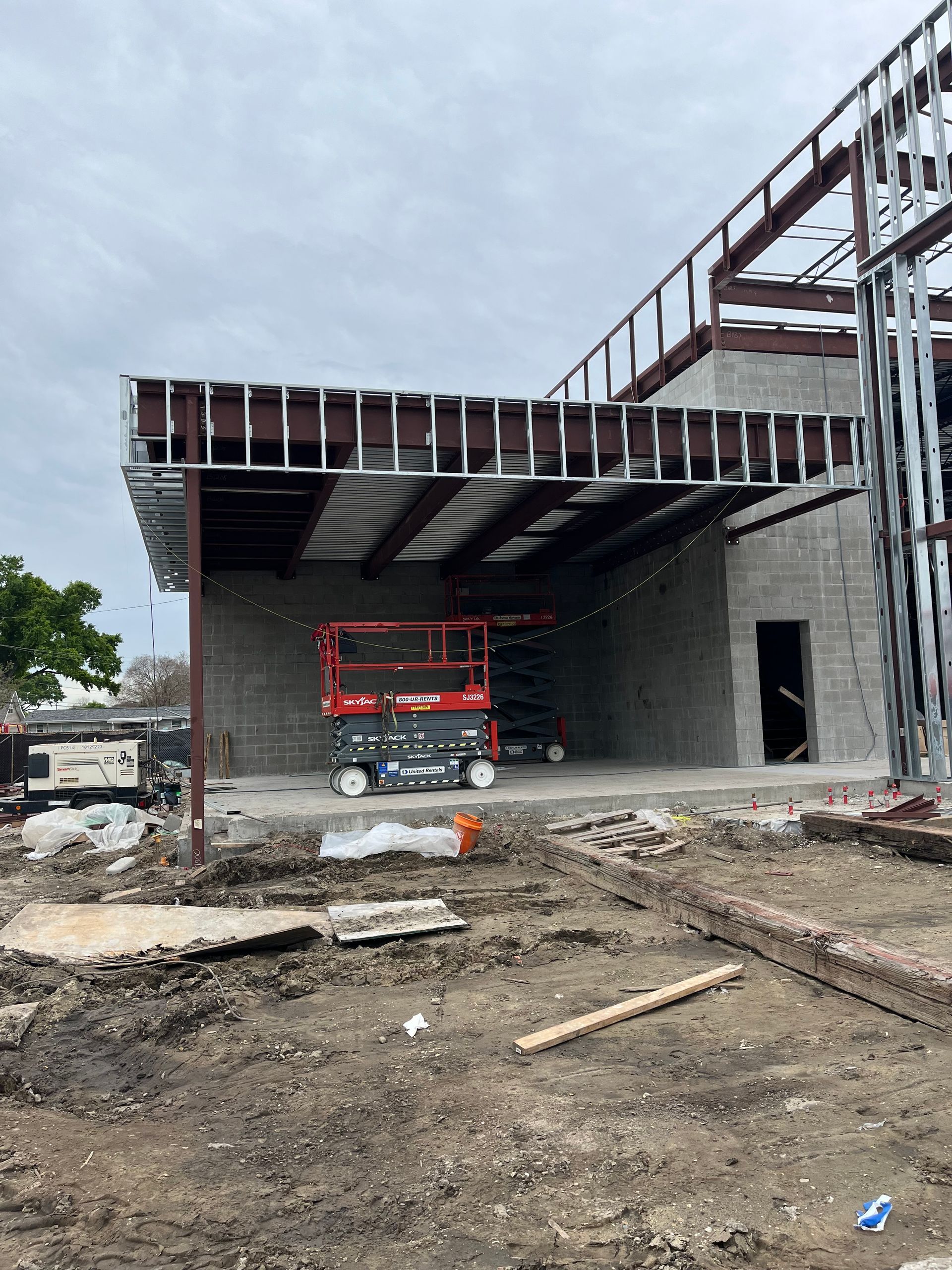 Construction site: metal building frame with a red lift inside a covered area. Cloudy sky.
