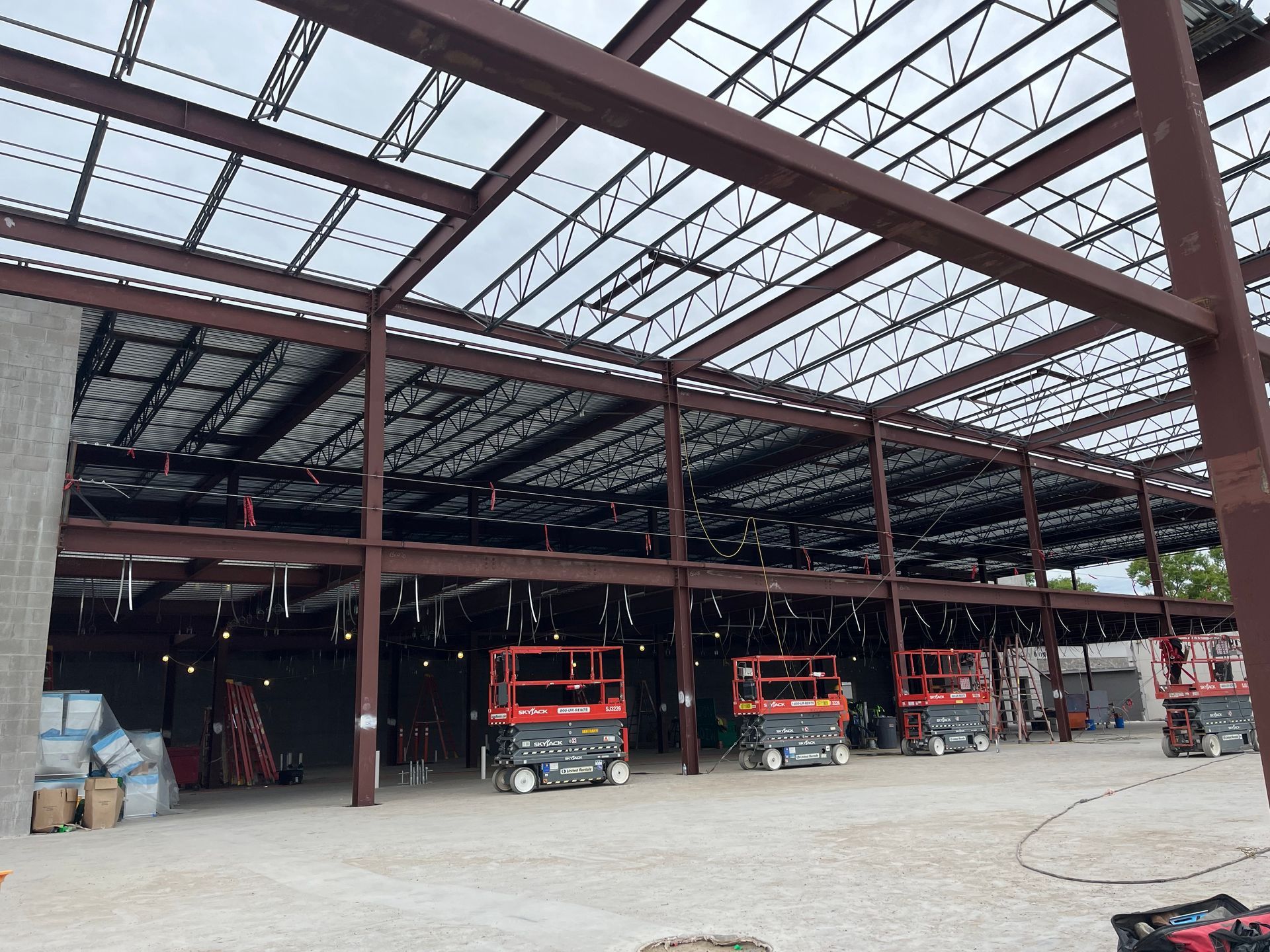 An interior view of a commercial building under construction with exposed steel beams and several red scissor lifts.