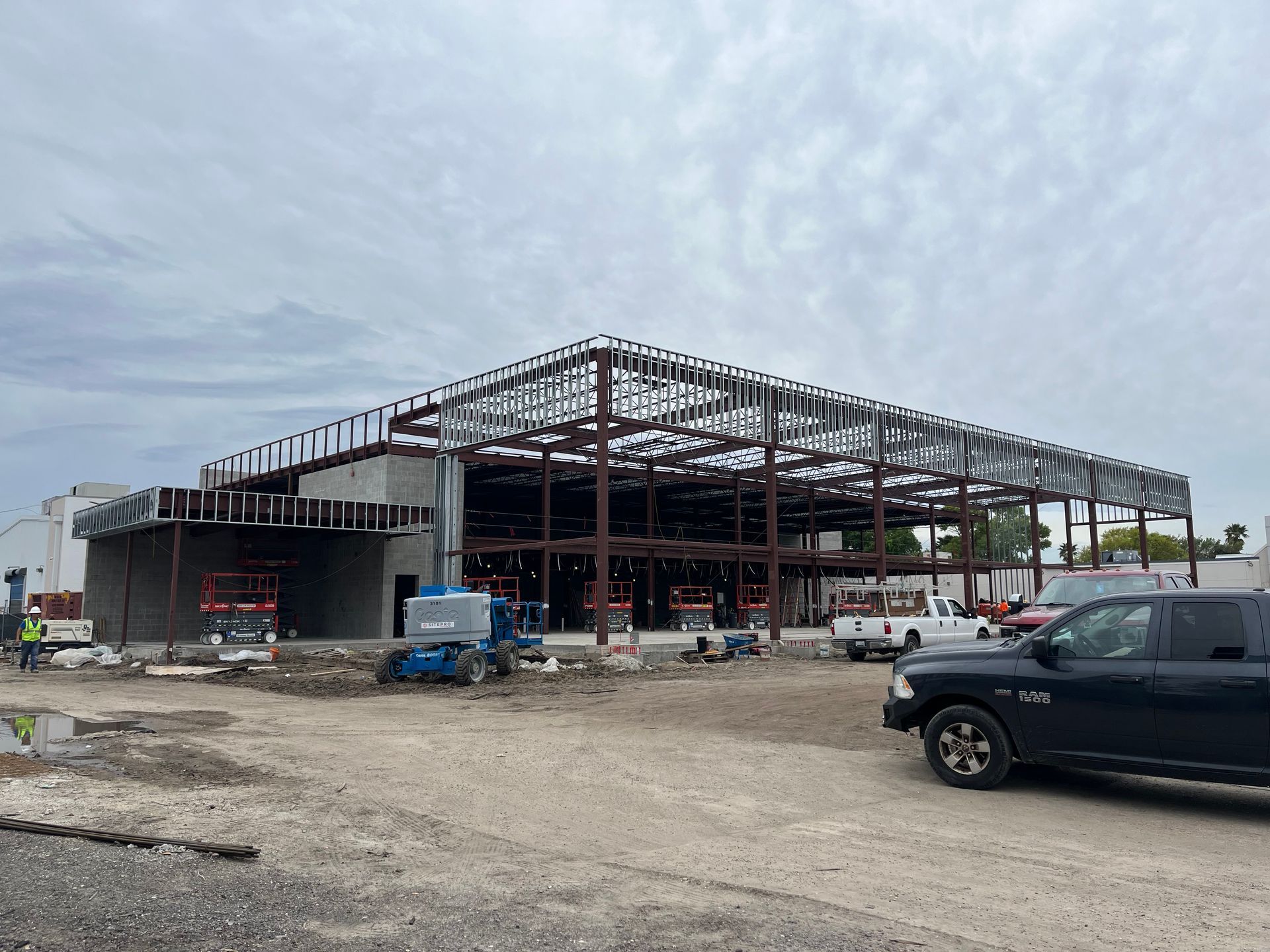 A commercial building under construction with a steel frame skeleton, concrete walls, and construction equipment outside.