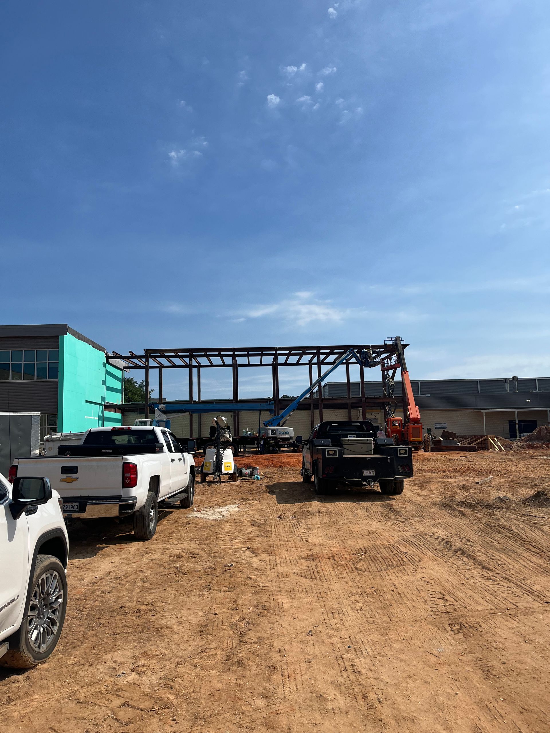 Construction site with steel beams, scaffolding, and rebar grid against a blue sky.