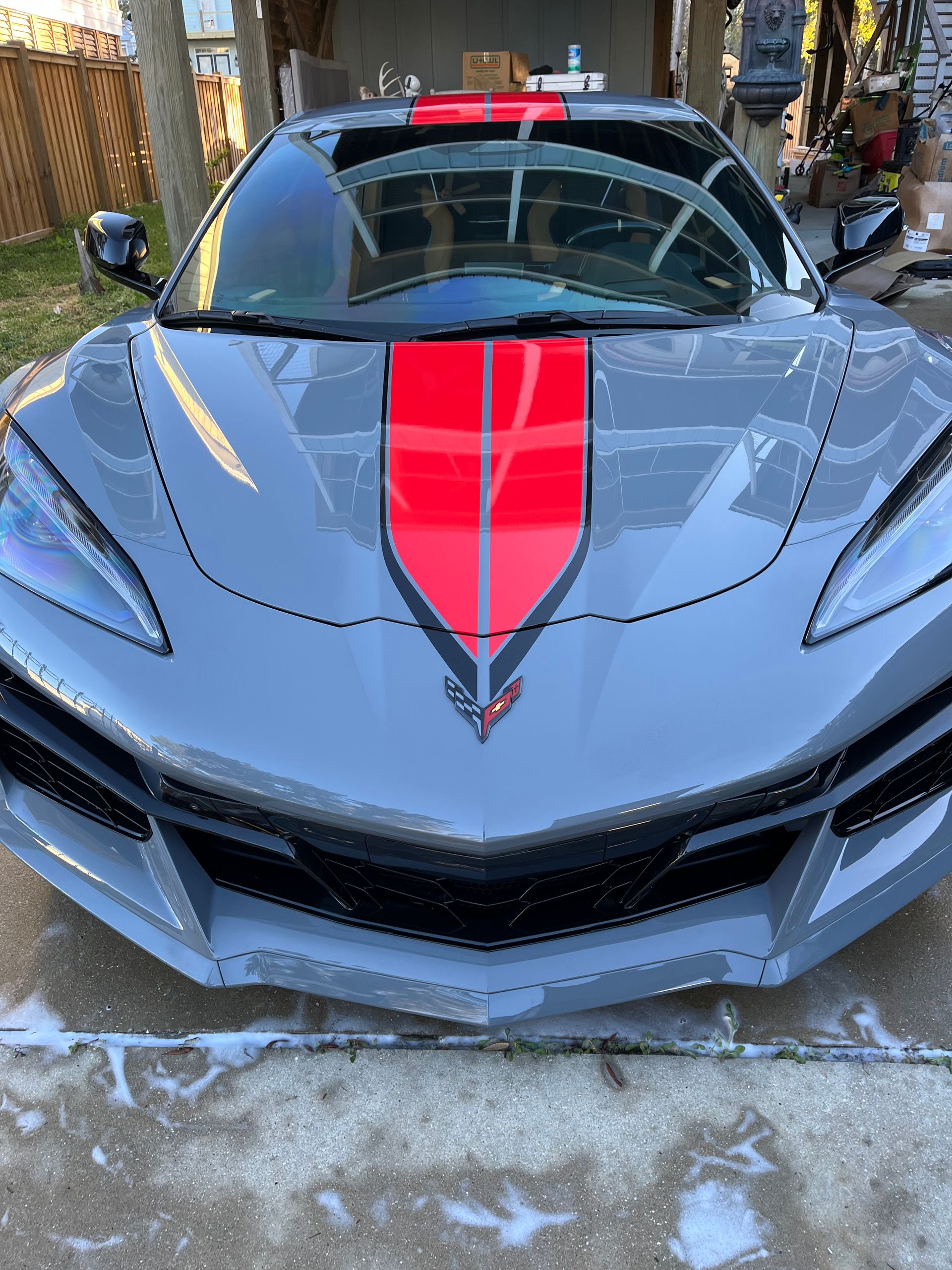 Man polishes a black car hood in a garage. Car is covered in plastic.