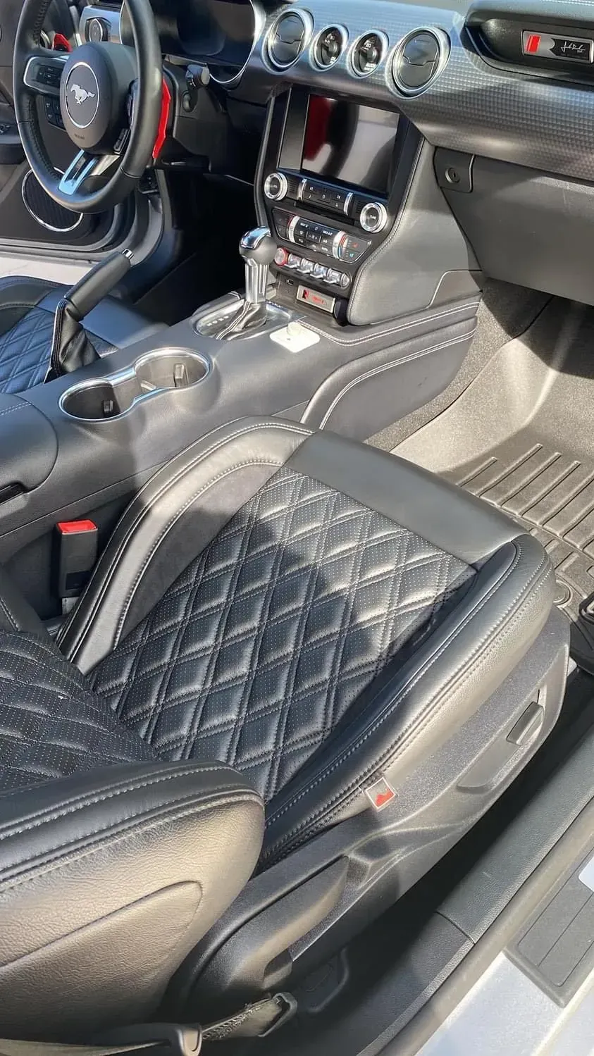 The interior of a Ford Mustang featuring black diamond-stitched leather seats, white piping, and a dark dashboard.