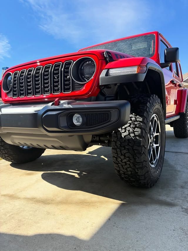 Red Jeep Wrangler, front view, outdoors on a sunny day.
