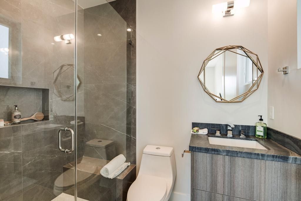 Modern bathroom with gray tiled shower, toilet, and vanity with an octagonal mirror.
