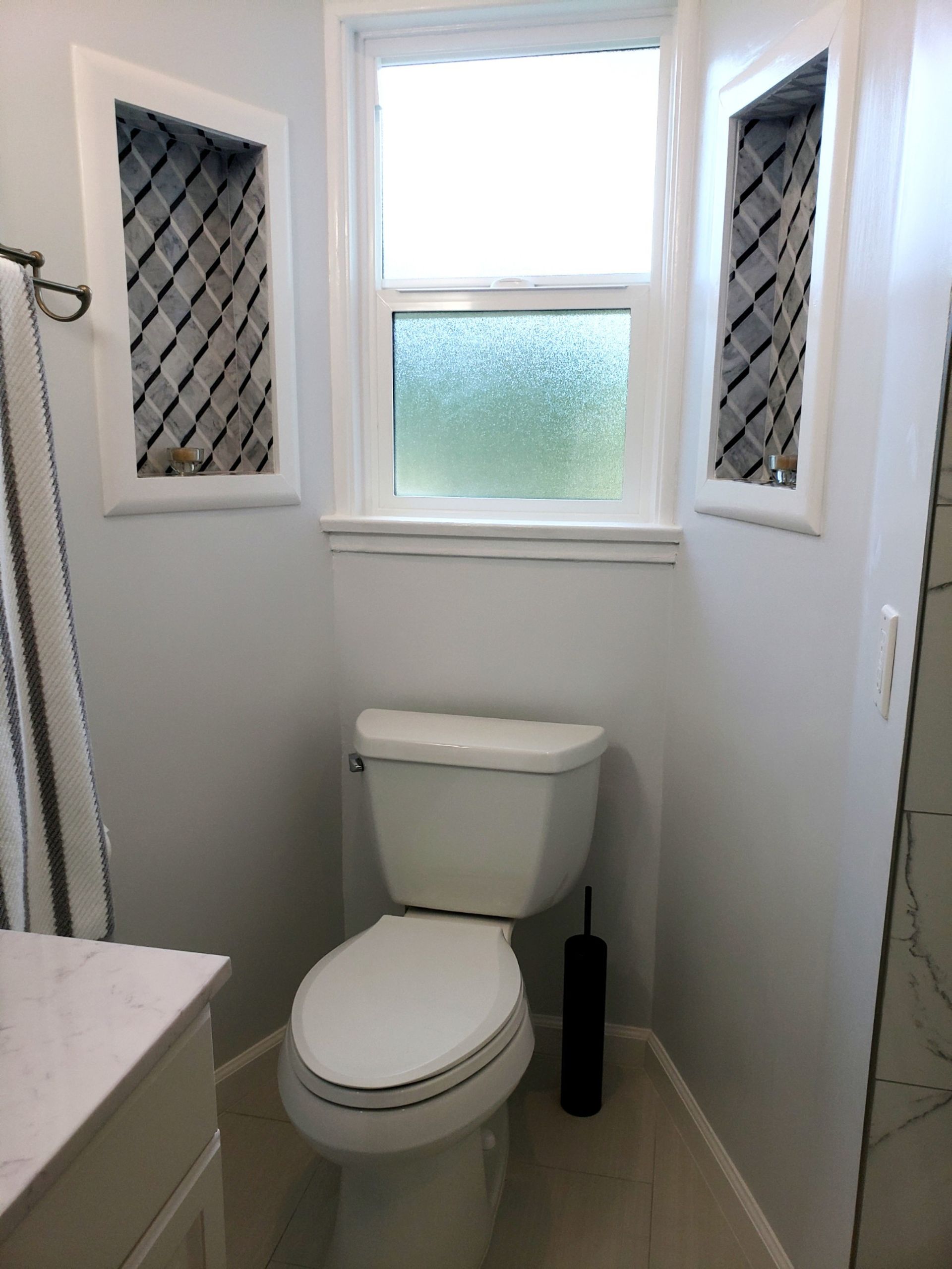 Bathroom with toilet, window, and decorative niches. Light gray walls, white trim.