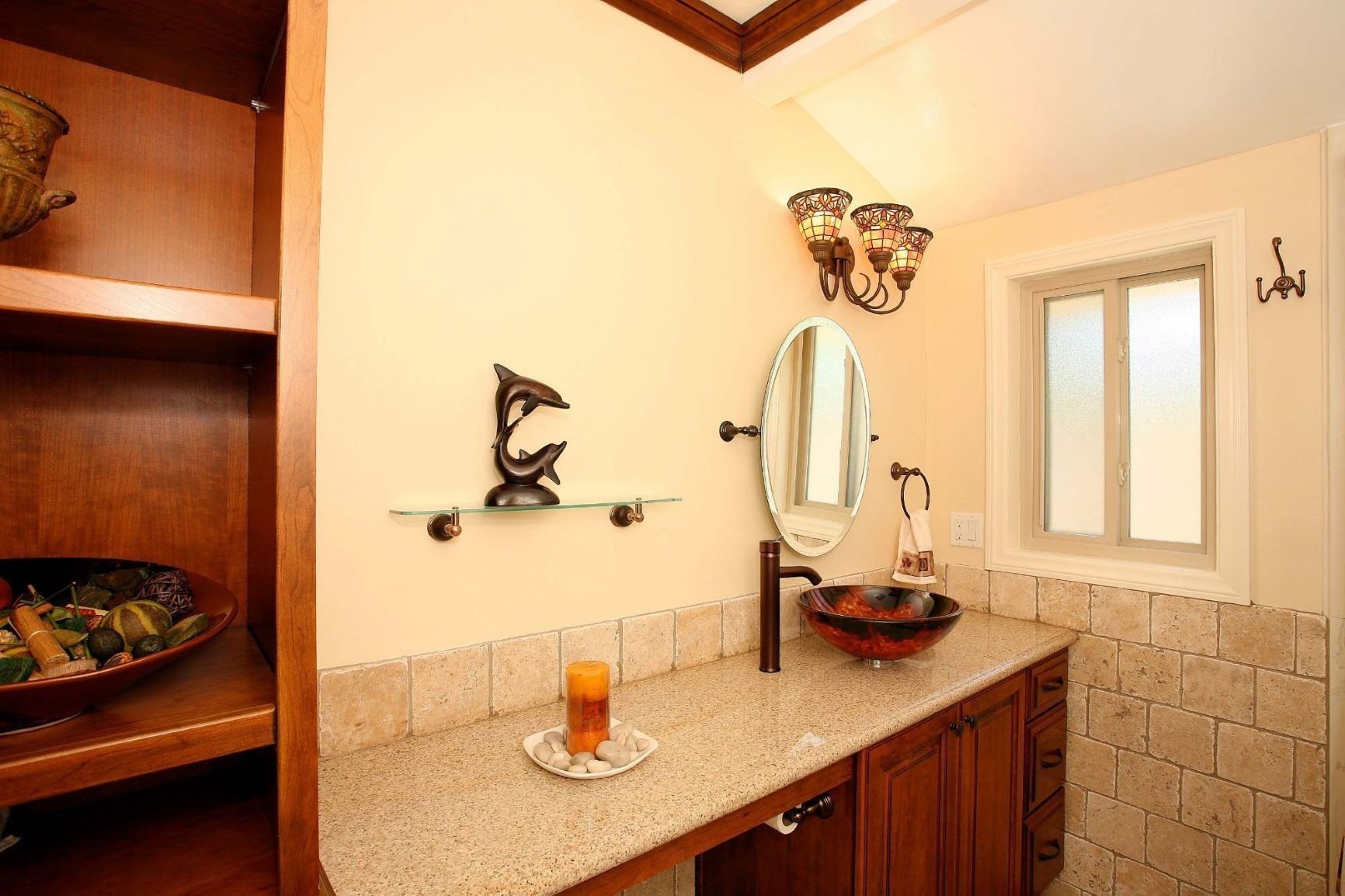Bathroom with a wooden vanity, granite countertop, glass sink, and a frosted window.