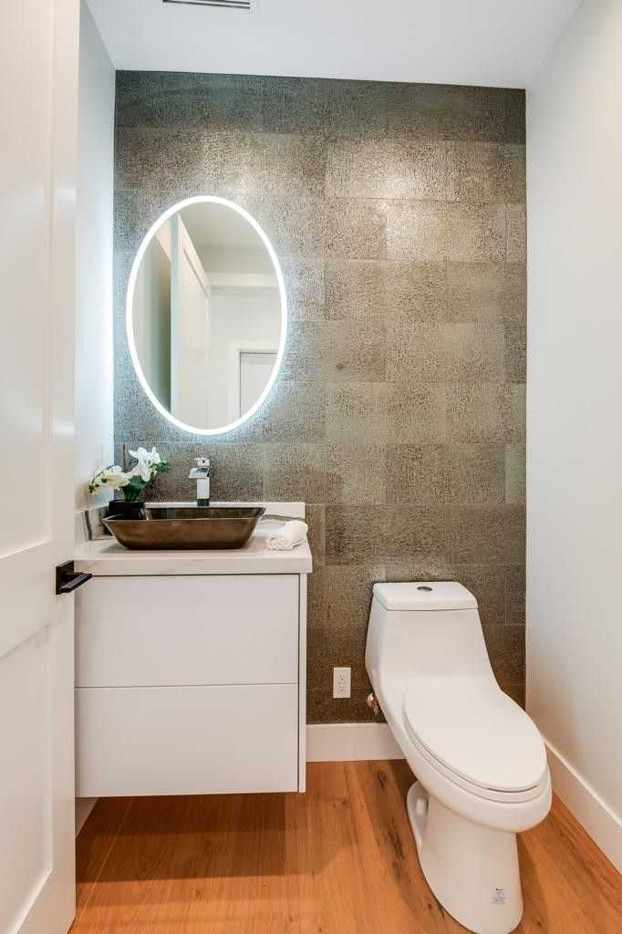 Modern bathroom with a textured gray wall, floating white vanity, oval mirror, and a white toilet.