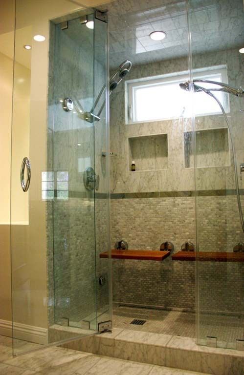 Spacious, tiled shower with glass doors, built-in benches, and multiple showerheads.