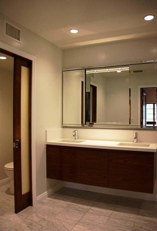 Modern bathroom with double sink, large mirror, and dark wood vanity; a sliding door is open to the toilet.