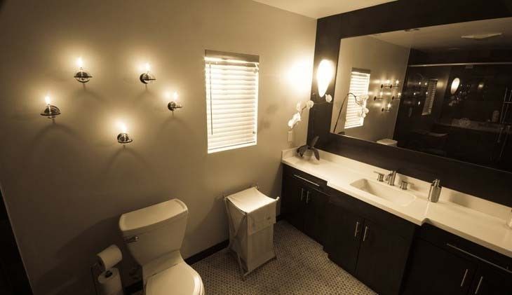 Bathroom with toilet, sink, mirror, decorative lights, and window with blinds.