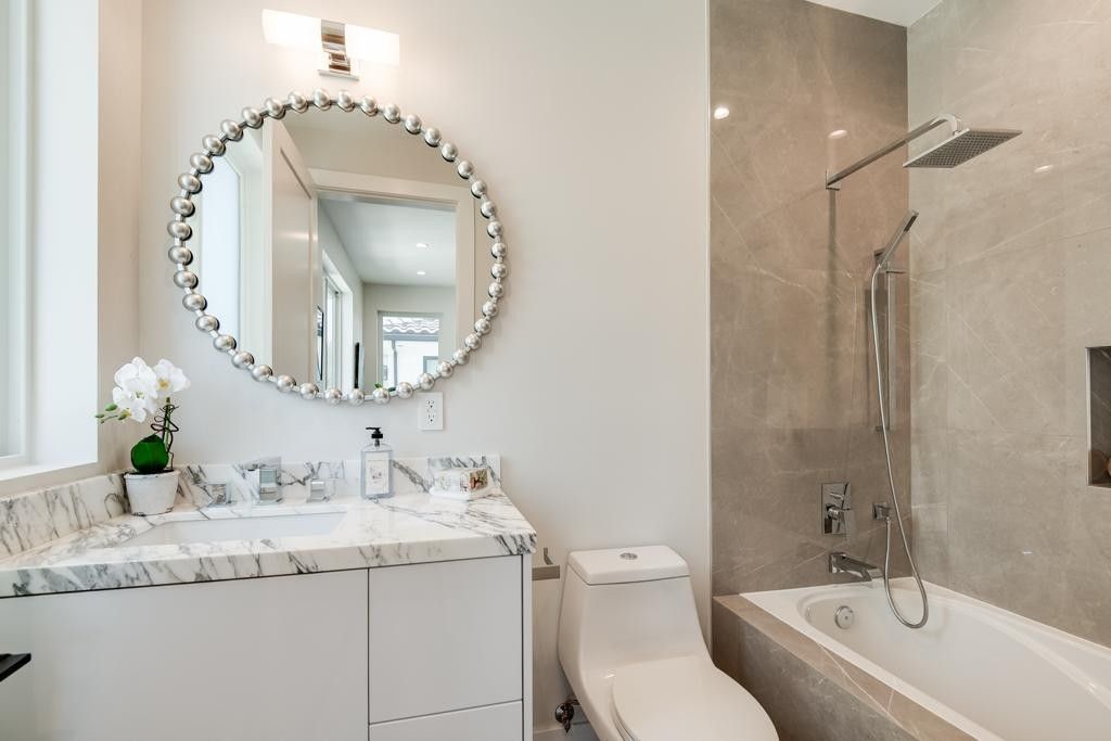 Bathroom with white vanity, toilet, and bathtub. Features marble countertops and gray tiled shower.