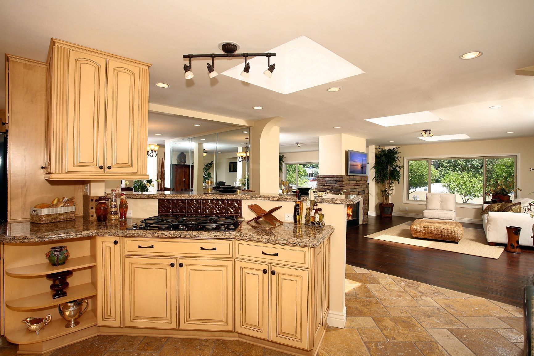 Kitchen with light-colored cabinets, granite countertops, and open layout to a living area with large windows.