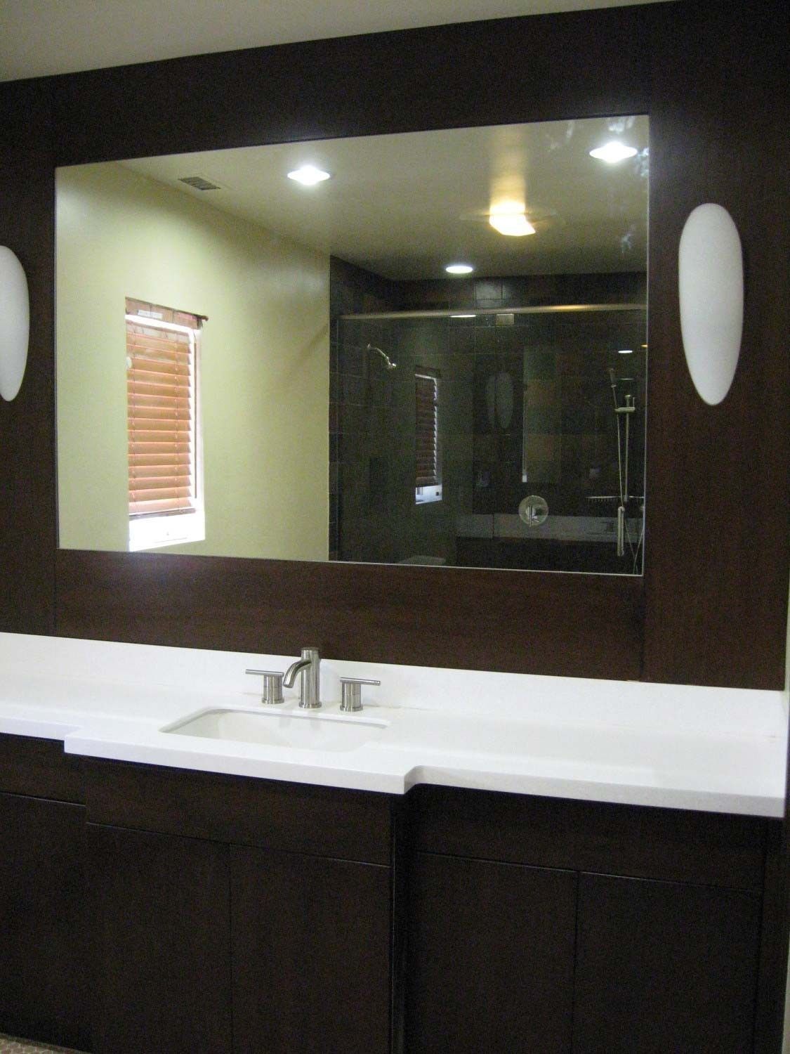 Bathroom vanity with a large mirror, dark cabinetry, and white countertop.