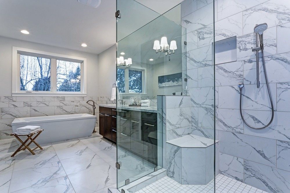Modern bathroom with marble tile, glass shower, and freestanding tub near window.