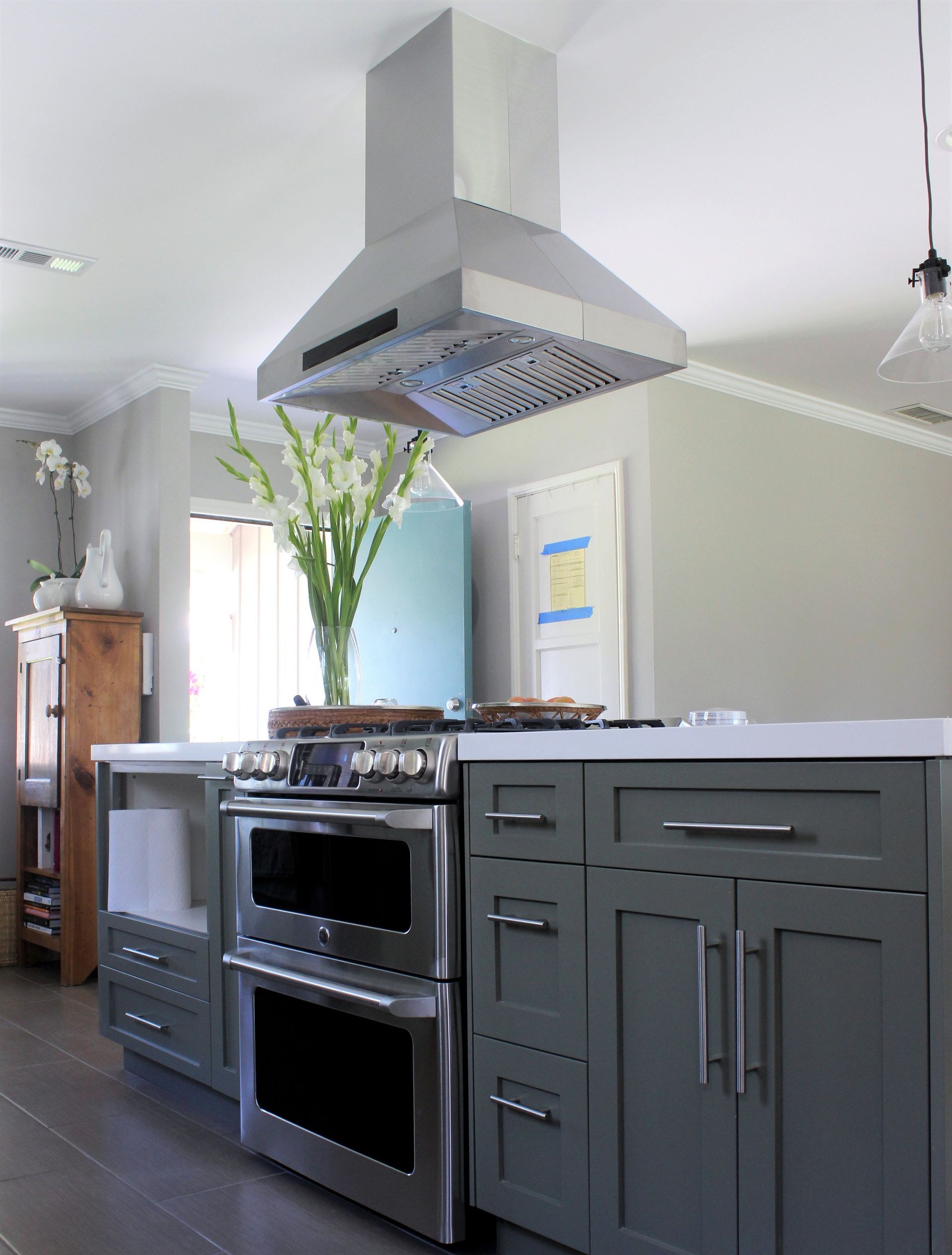 Gray kitchen island with oven, cabinets, range hood, and tall flower vase.