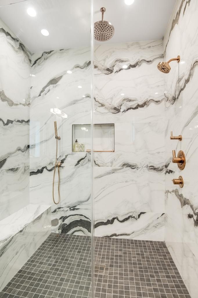 Marble-tiled shower with a glass door, overhead and handheld showerheads, and a tiled floor.