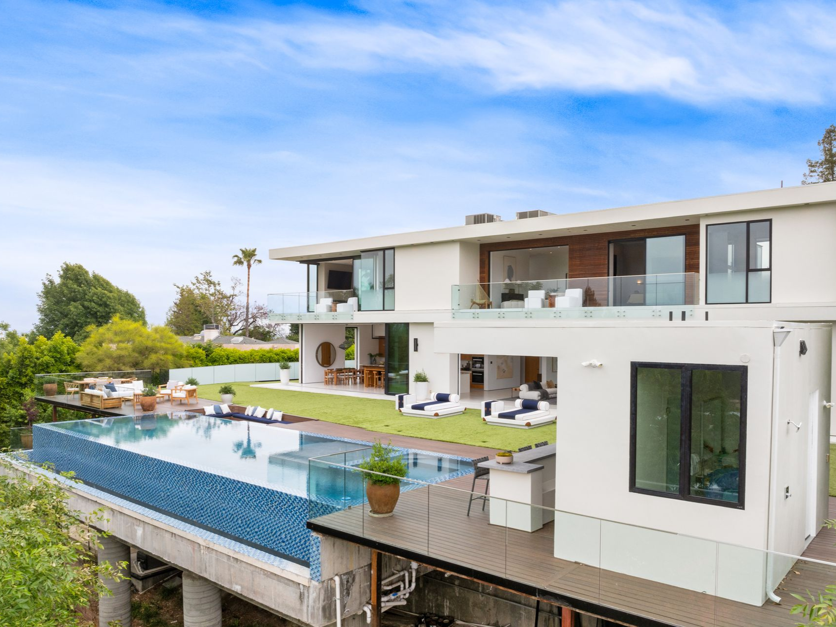 Modern white house with infinity pool overlooking landscape, sunny day.