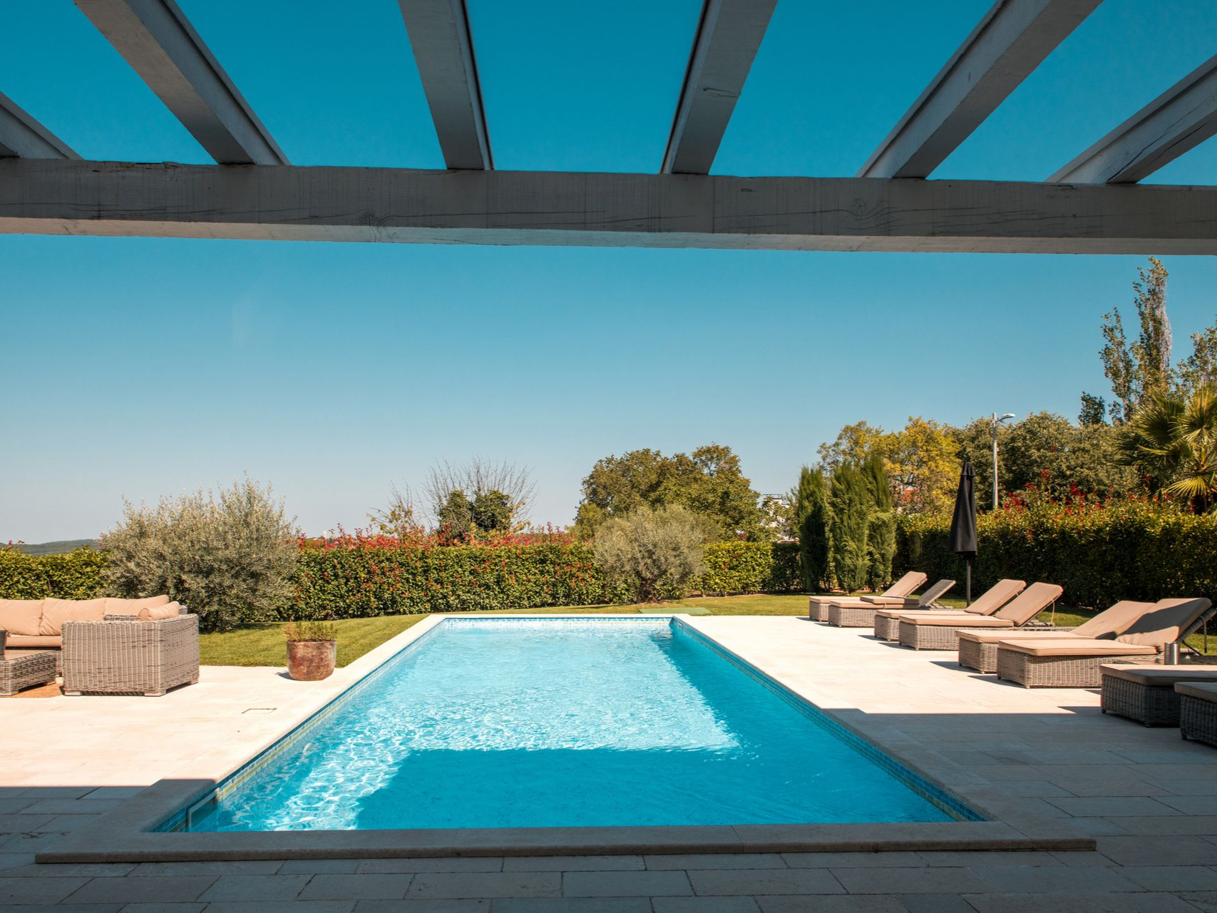 Pool with lounge chairs under pergola on sunny day.