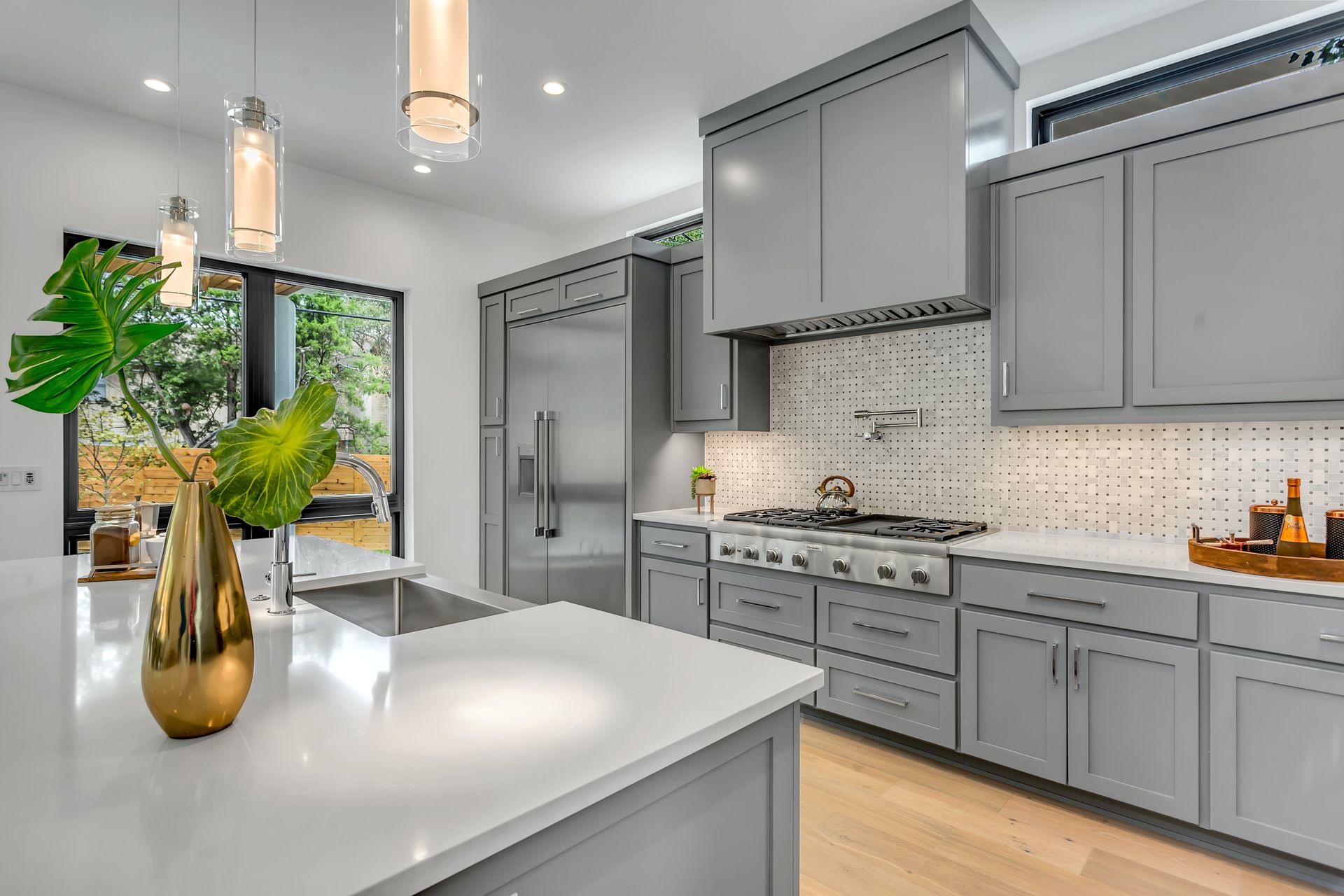 Modern kitchen with gray cabinets, stainless steel appliances, white countertops, and wood floor.