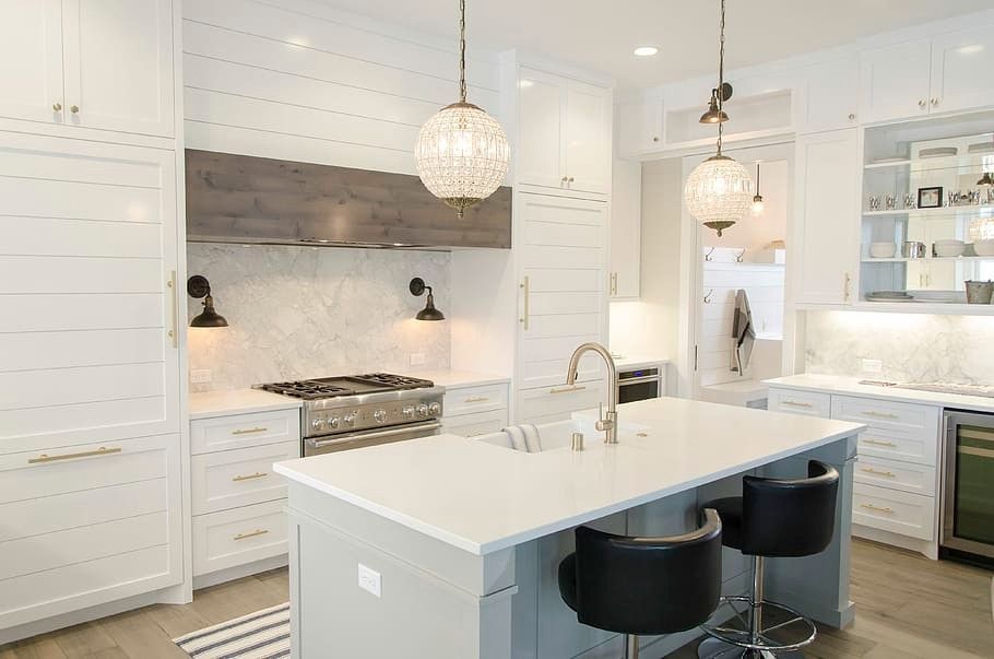 Modern white kitchen with island, range, and two crystal pendant lights.