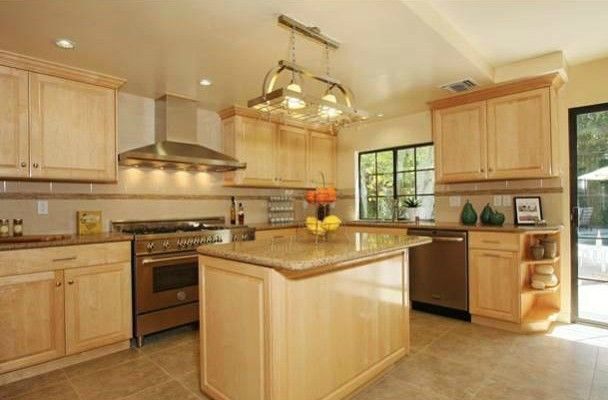 Bright, well-lit kitchen with light wood cabinets, stainless steel appliances, and a central island with granite countertop.