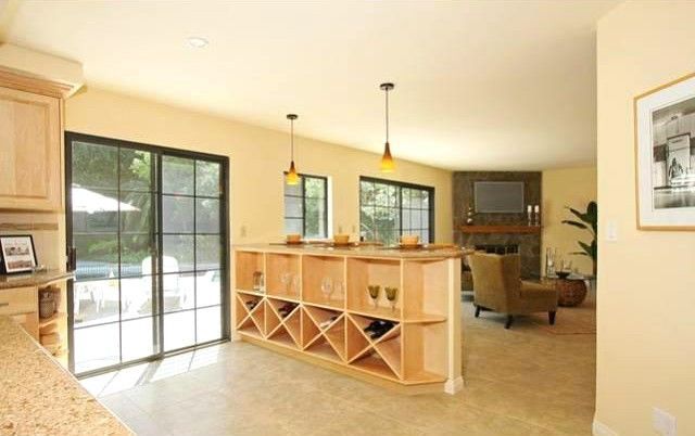 Open-concept kitchen and living area, island wine rack, sliding glass door to pool, fireplace, neutral tones.