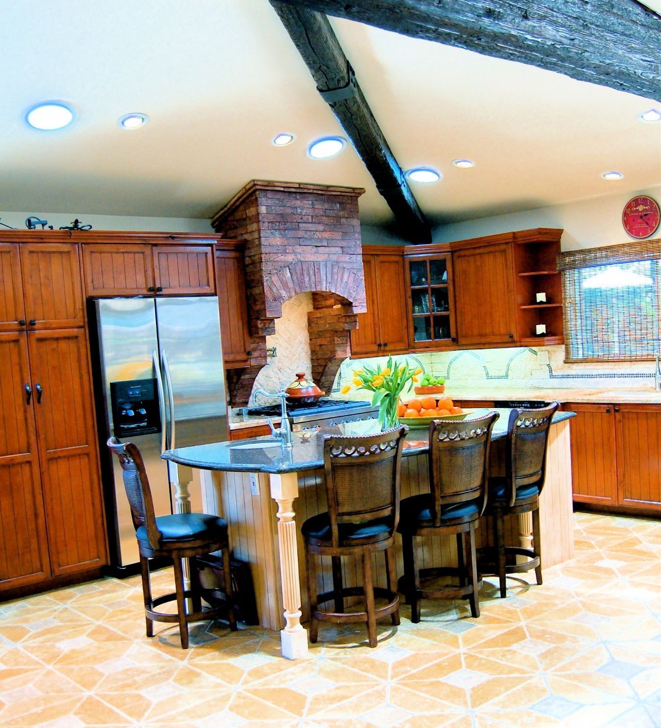 Kitchen with wooden cabinets, island with seating, stainless steel fridge, and stone range hood.