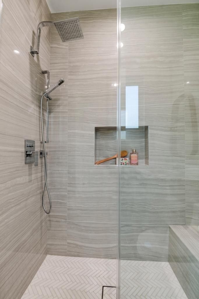Modern shower with gray tiled walls, glass door, and built-in shelf.