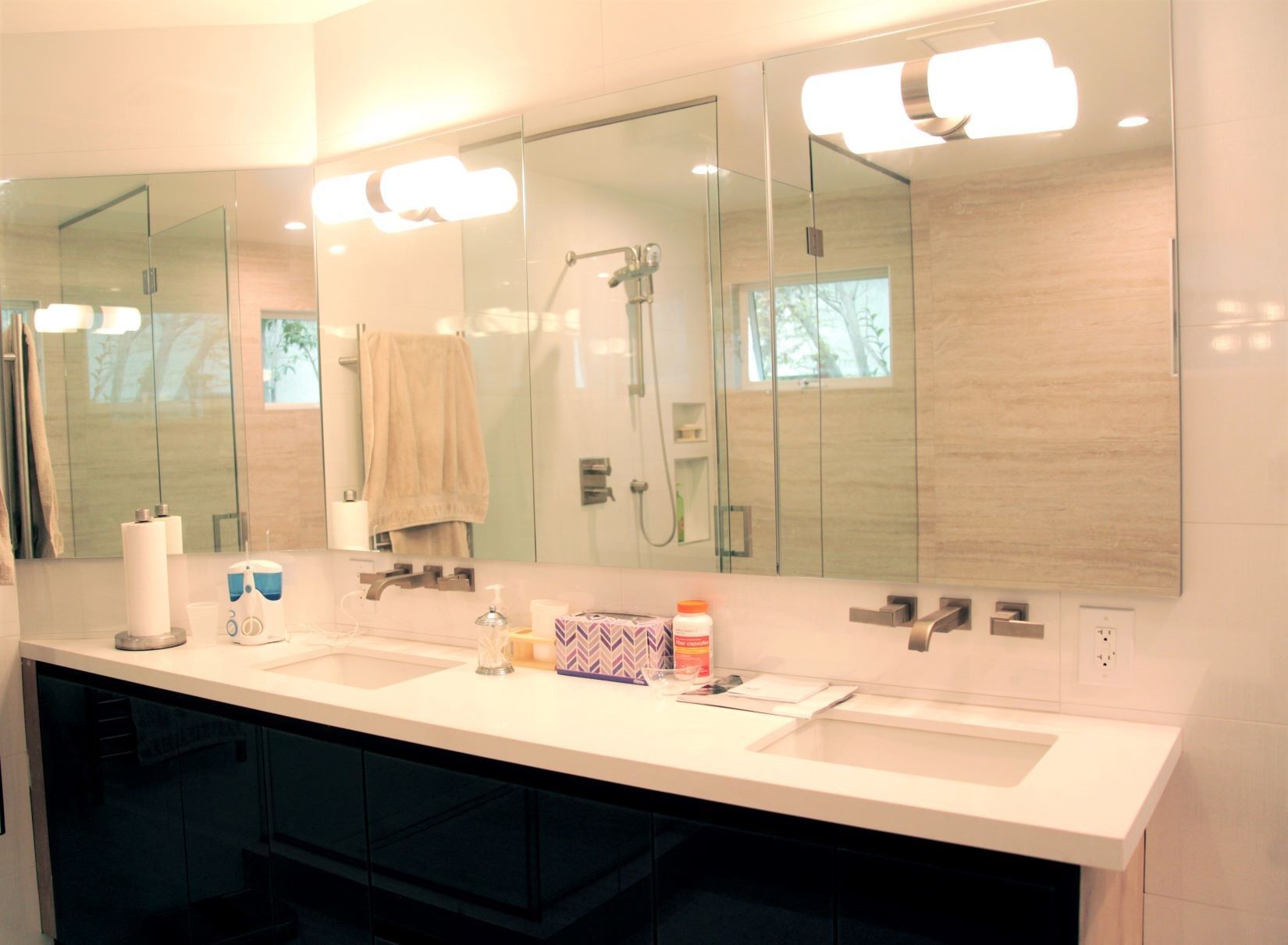 Modern bathroom with white countertops, black cabinets, and large mirrors.