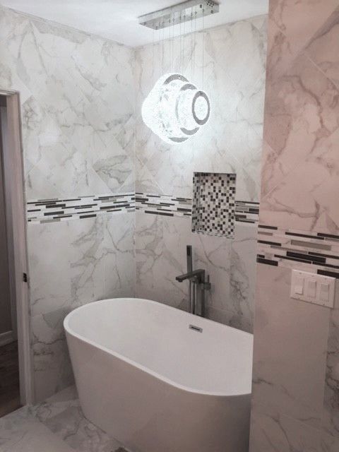 Modern bathroom with a white freestanding tub, marble-patterned walls, and a decorative light fixture.
