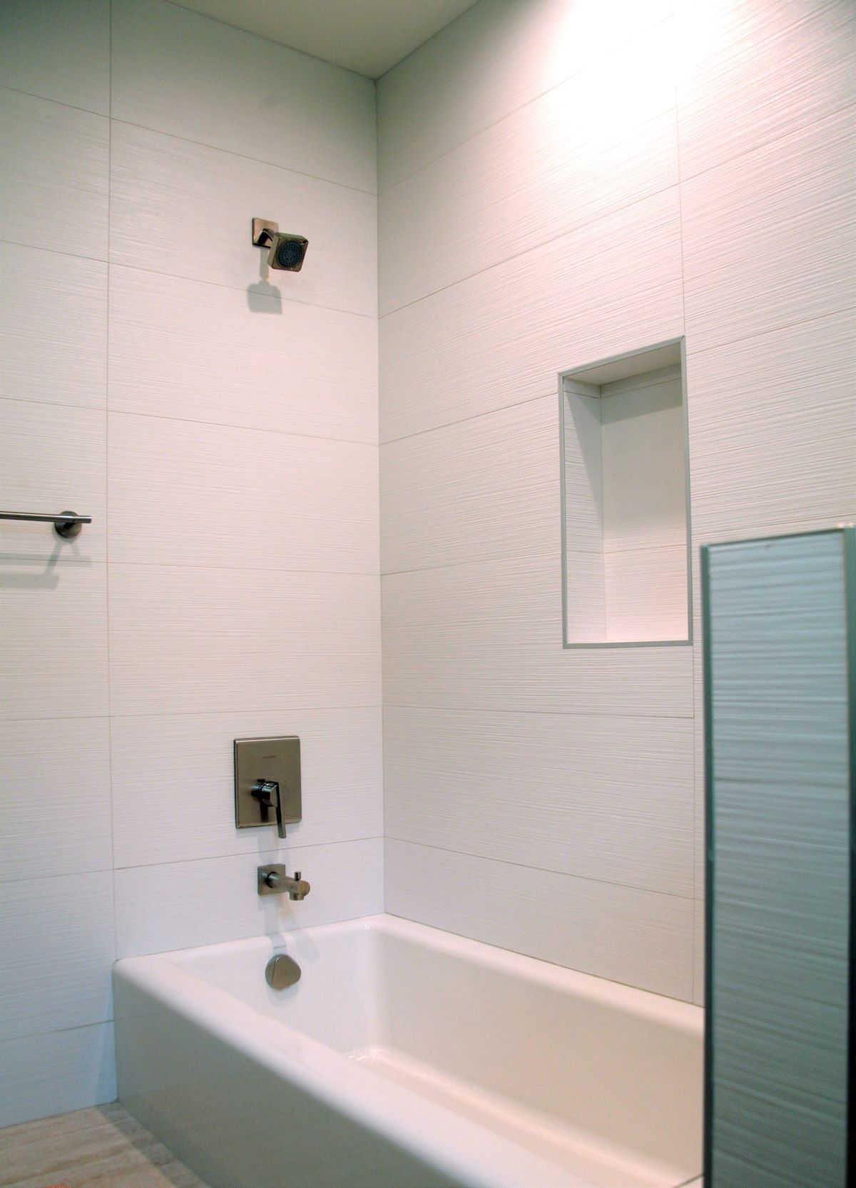 White-tiled bathroom with a bathtub, showerhead, and recessed shelf.