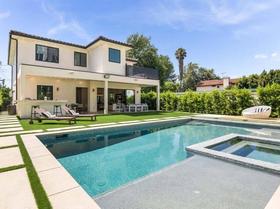 Backyard with pool, lounge chairs, and two-story house with patio, and green lawn on a sunny day.