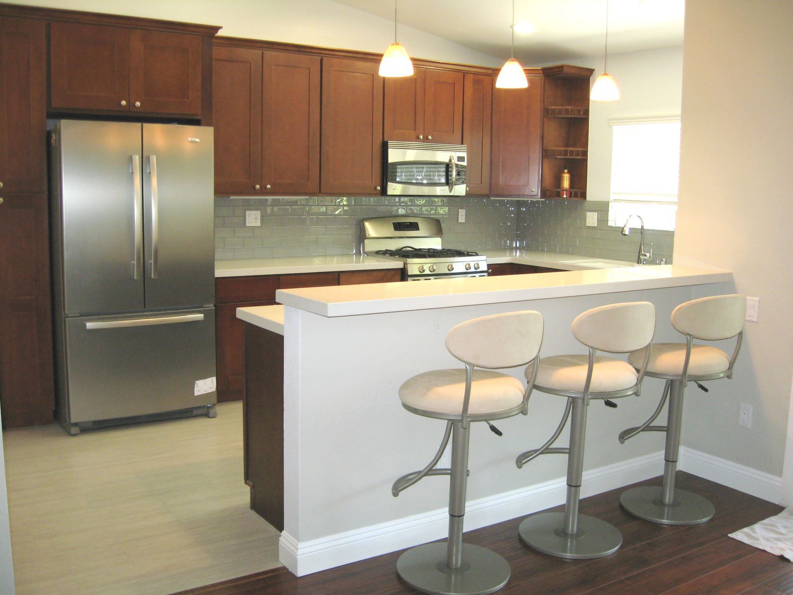 Kitchen with dark wood cabinets, stainless steel appliances, and a breakfast bar with three stools.