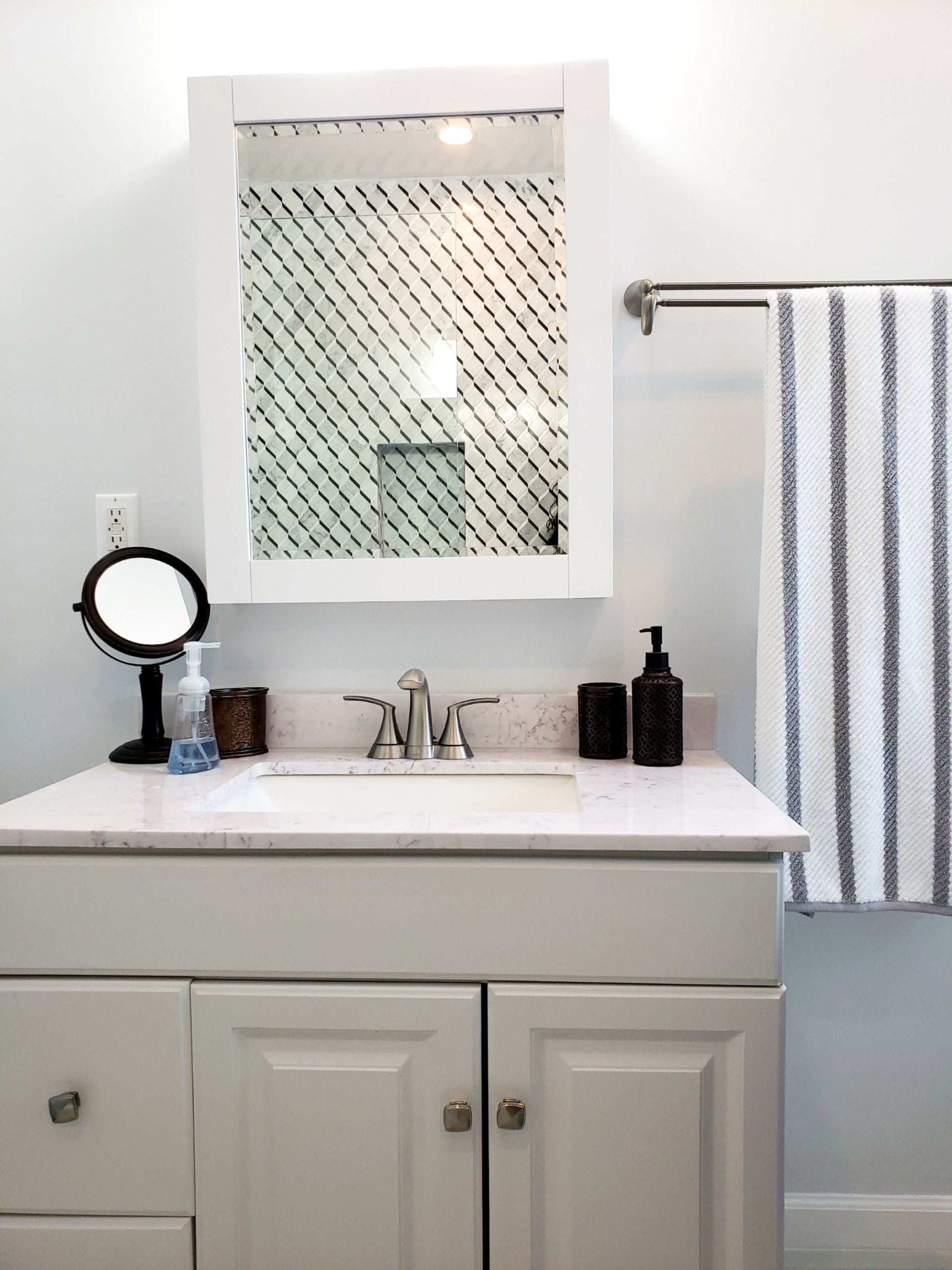 Bathroom vanity with a white cabinet, mirror, and striped towel.