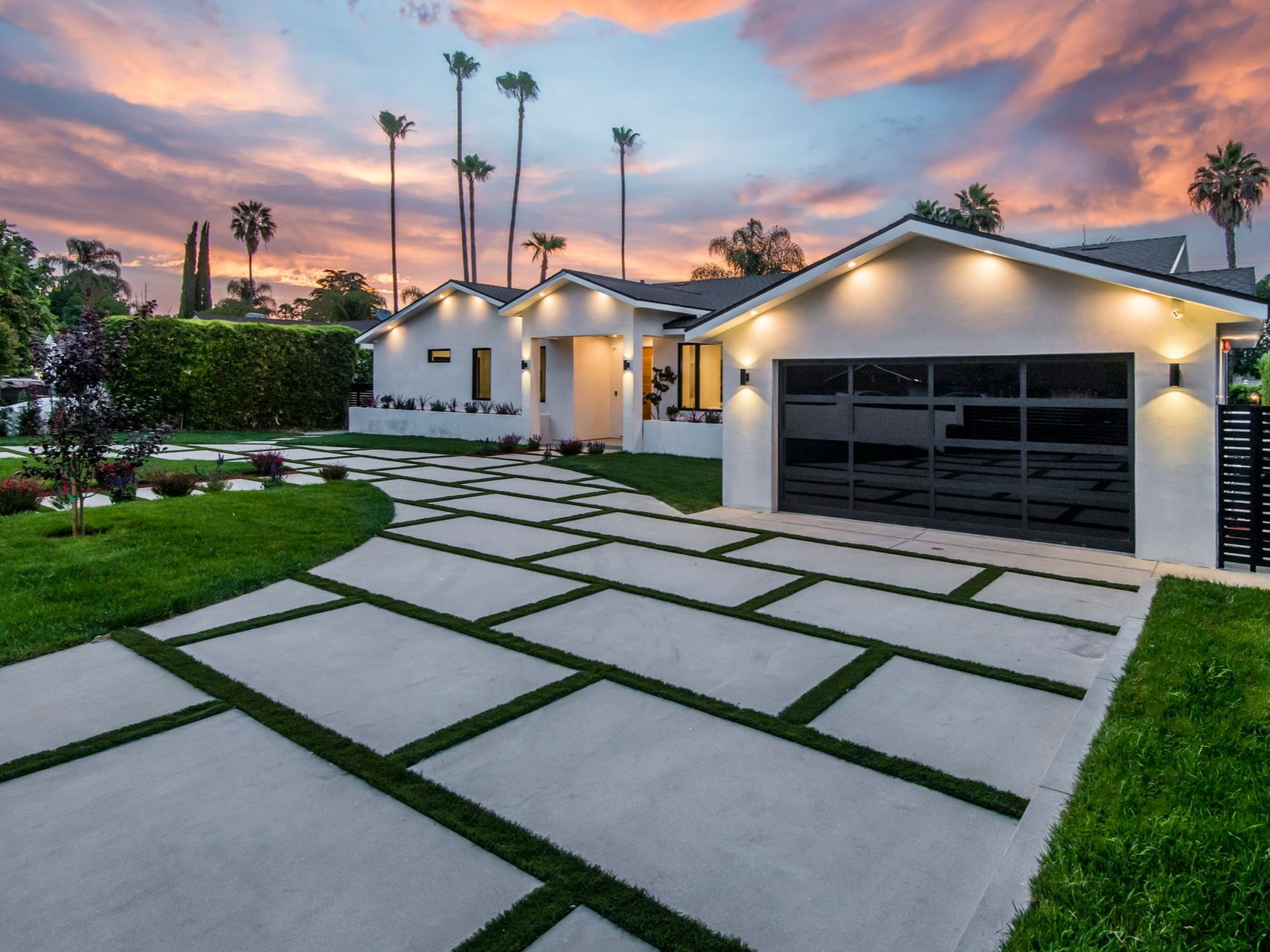 Modern home with a concrete driveway and lawn, against a colorful sunset sky.