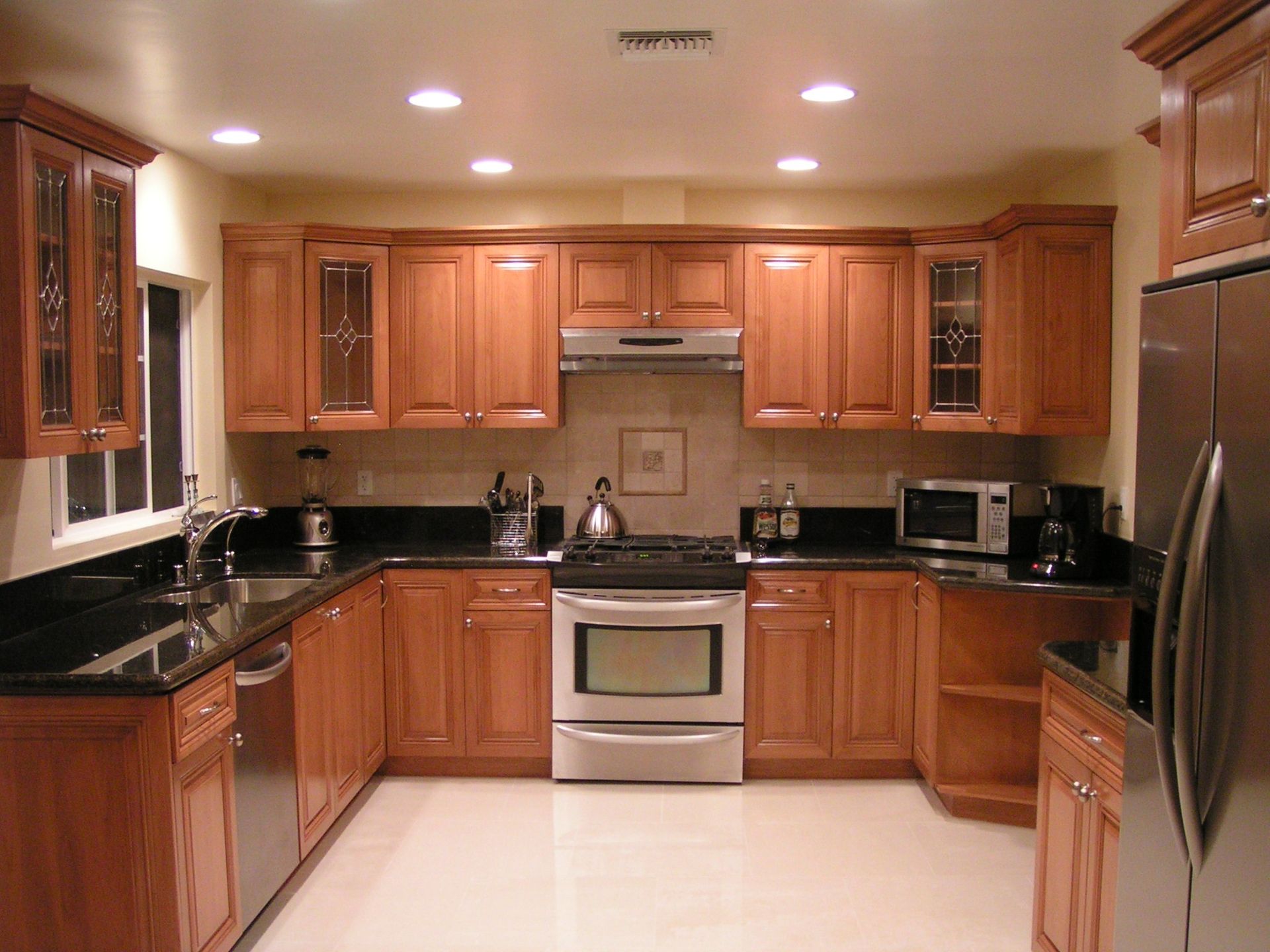 U-shaped kitchen with brown cabinets, black countertops, stainless steel appliances, and off-white tile floor.