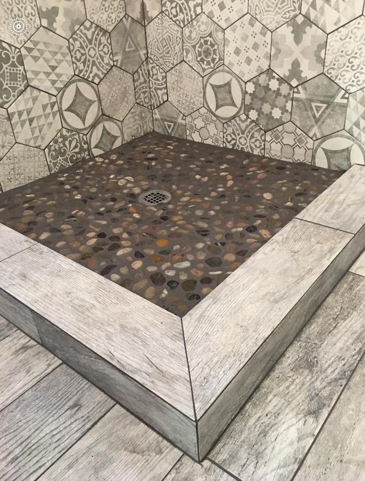 Shower with pebble tile floor and gray hexagonal wall tiles.